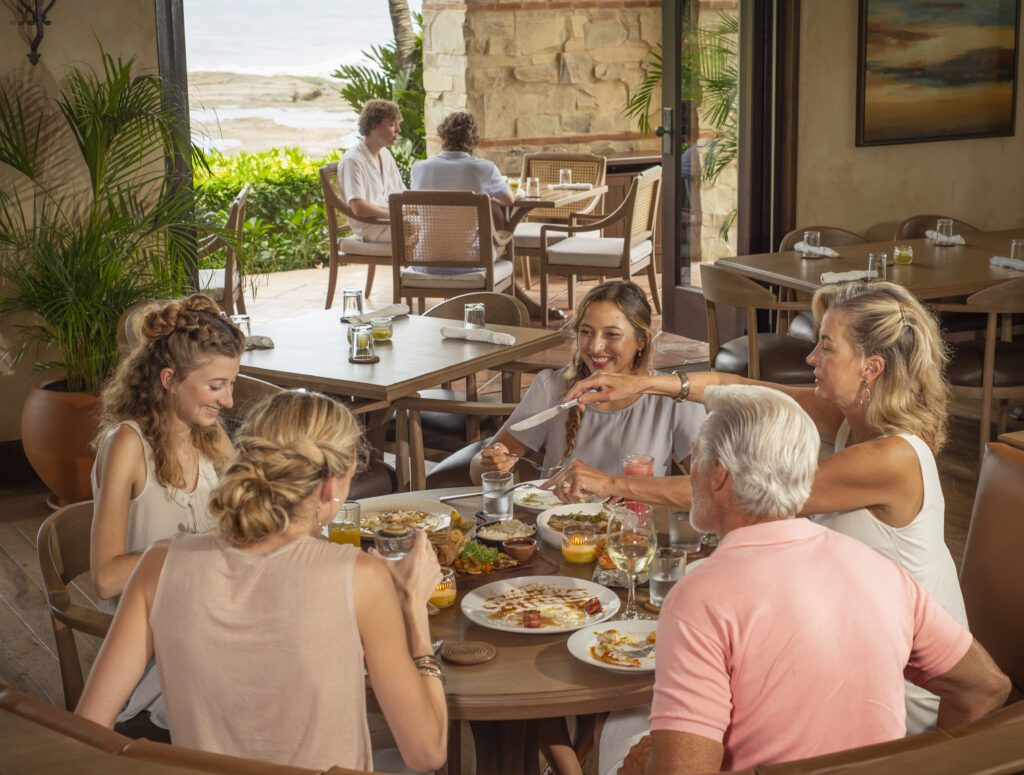 Family gathered around a table enjoying a meal at Rancho Santana family beach resort.